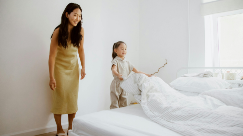 mãe ensinando a filha a arrumar a cama